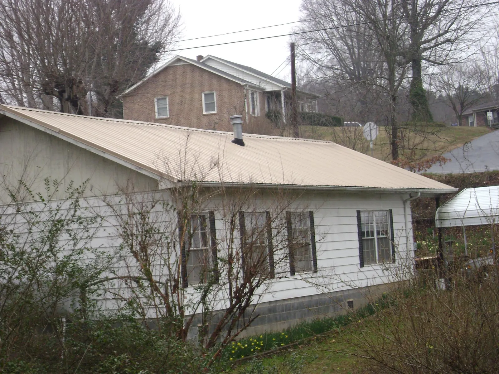 Tan metal roof on a white sided house set into a hillside — Commercial Roofing by Roofing Brothers in Tokeland